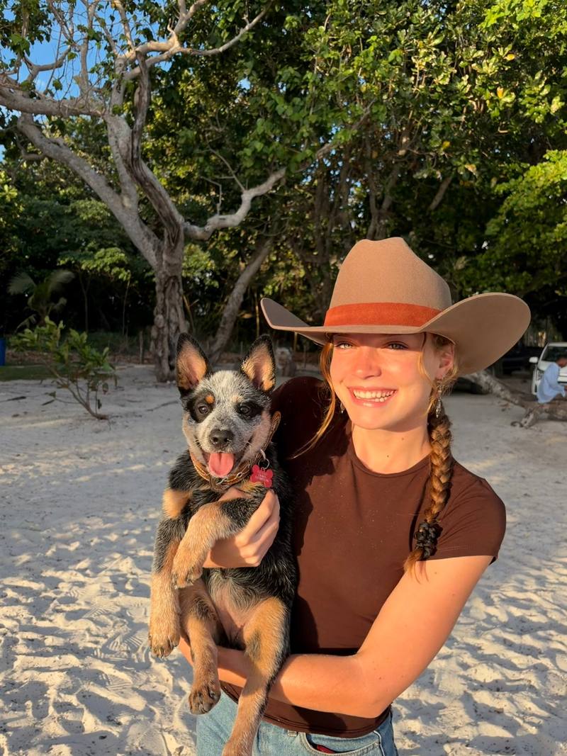 Emma in a felt cowboy hat on the beach, holding her cattle dog pup Pepper