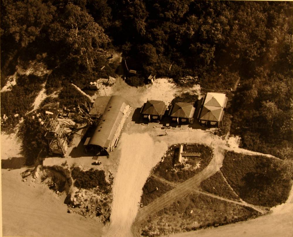 Overhead view of a Quonset hut, three tents and a tower at the edge of the strip